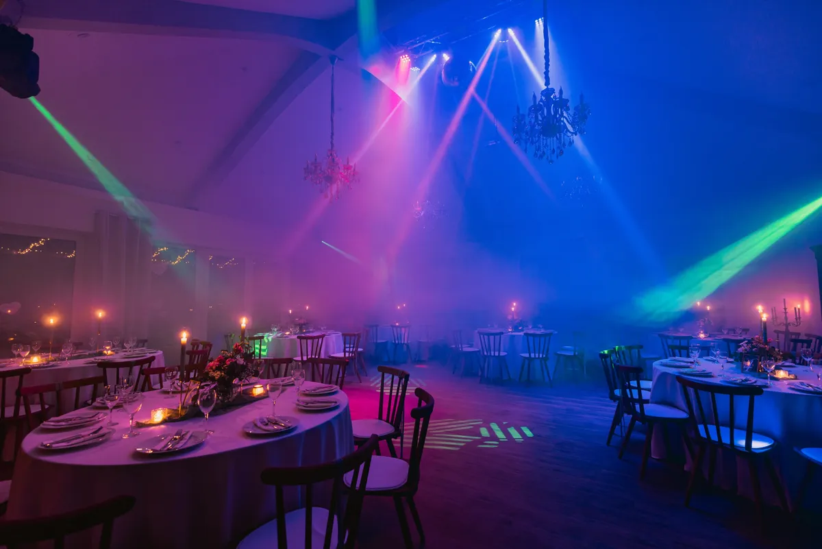 Grüne und blaue Lichtstrahlen kreuzen sich im vernebelten Festsaal über der Tanzfläche