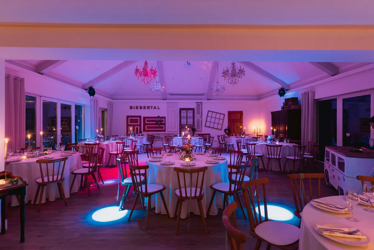 Festsaal bei Nacht in rosa-blauem Eventlicht mit angestrahlten Kronleuchtern und gedeckten runden Tischen