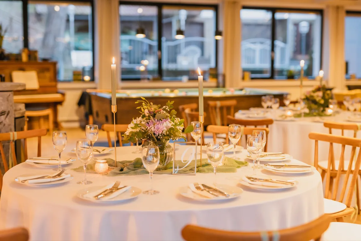 Gedeckter Tisch mit Tischnummer im Festsaal, dahinter Fensterfront und Billardtisch