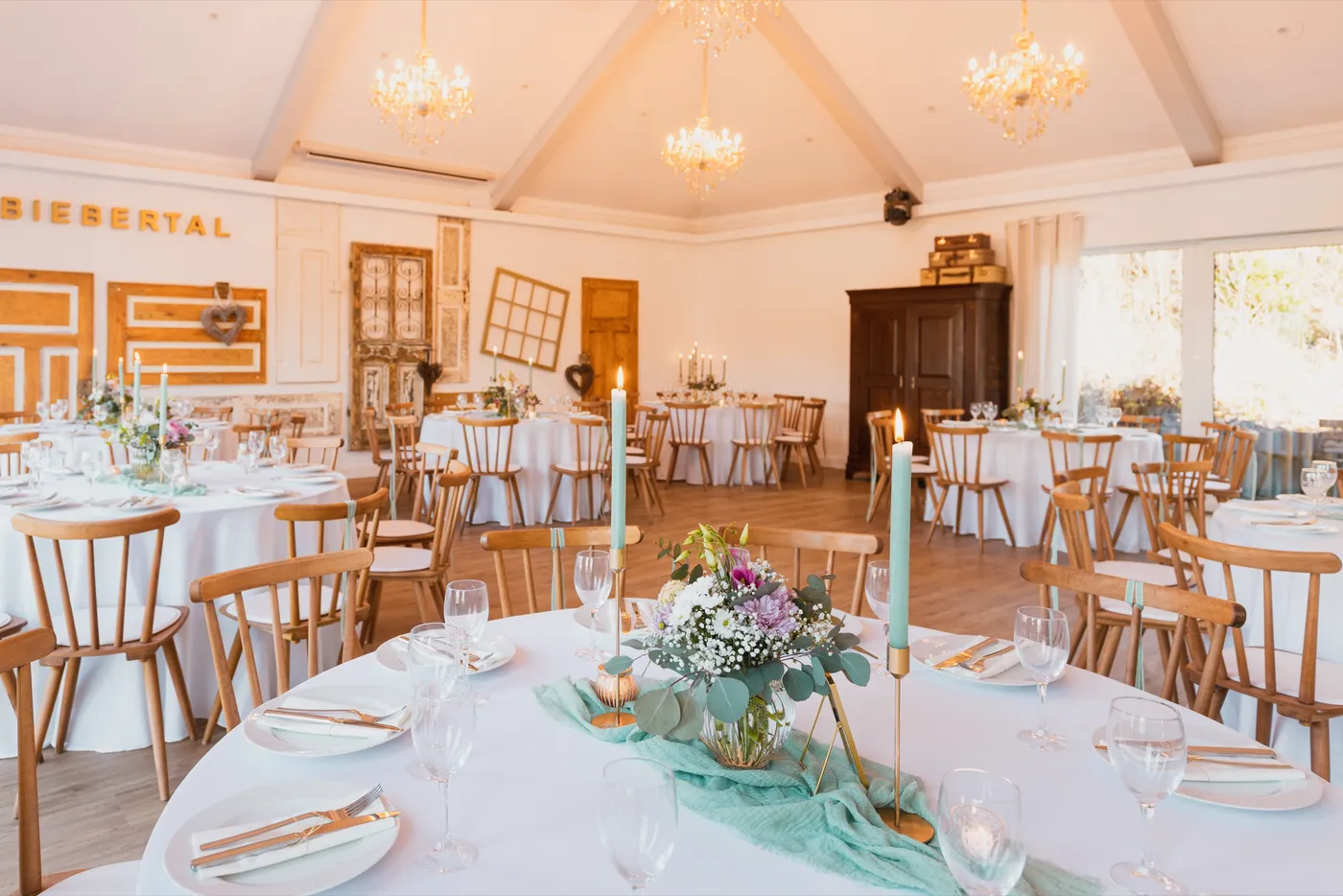 Festsaal mit antiker Türenwand, Kronleuchtern und Tafel mit mintgrüner Kerzendeko