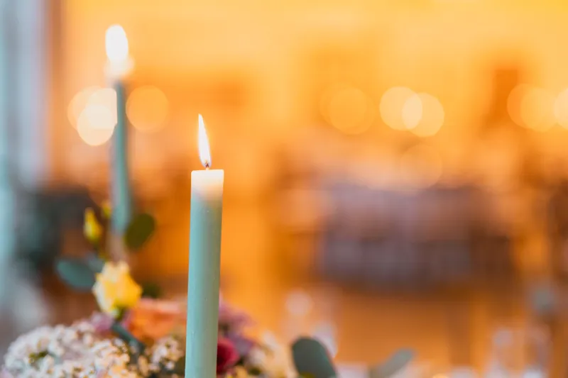 Brennende grüne Stabkerze mit Blumengesteck vor goldenem Bokeh im Festsaal