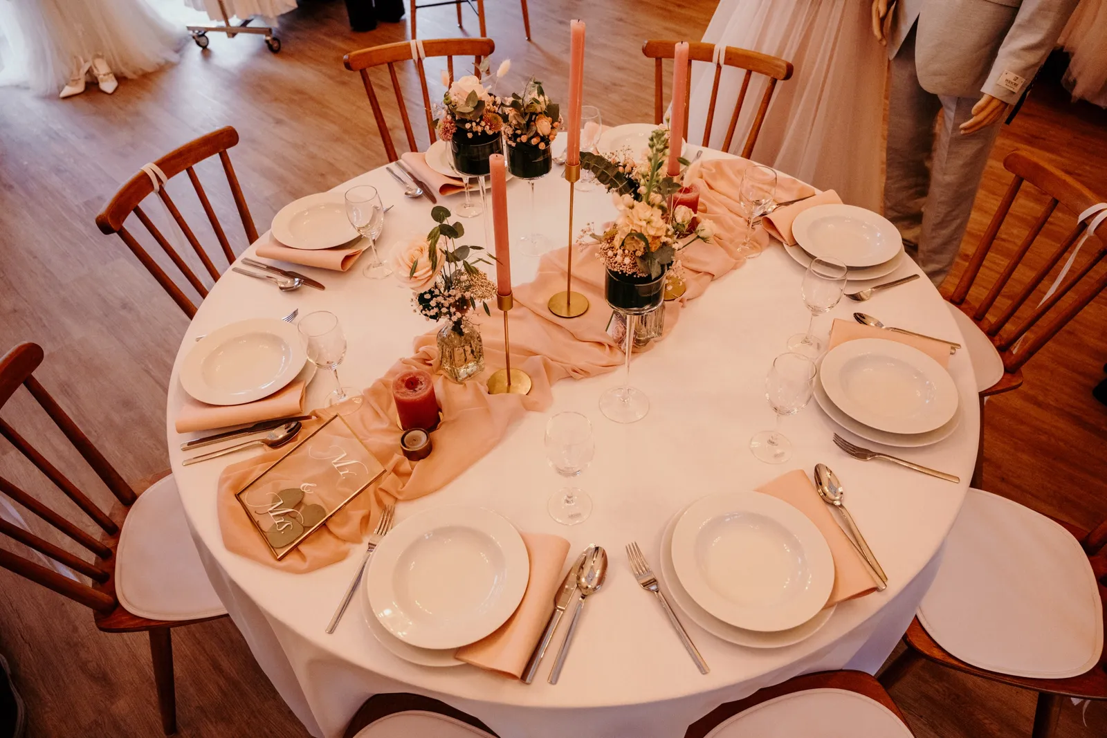 Rund eingedeckte Hochzeitstafel mit apricotfarbener Deko, rosé Kerzen und Blumen von oben