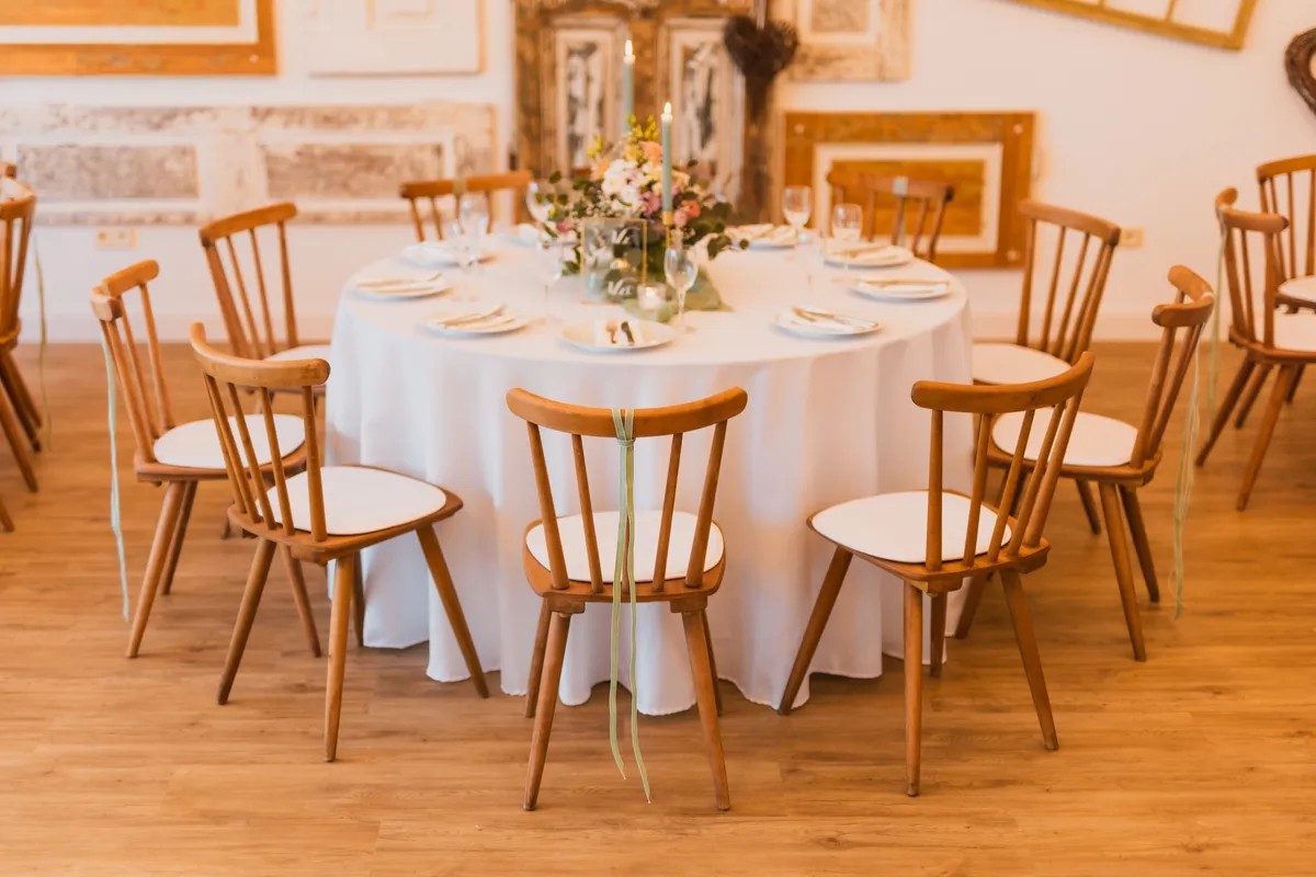 Rund eingedeckter Hochzeitstisch mit Holzstühlen und Blumengesteck vor Wand mit antiken Türen