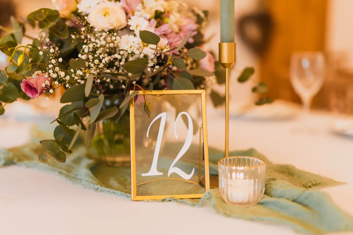 Tischnummer 12 im Goldrahmen mit Pastellblumen, Kerze und Windlicht auf salbeigrünem Tischläufer